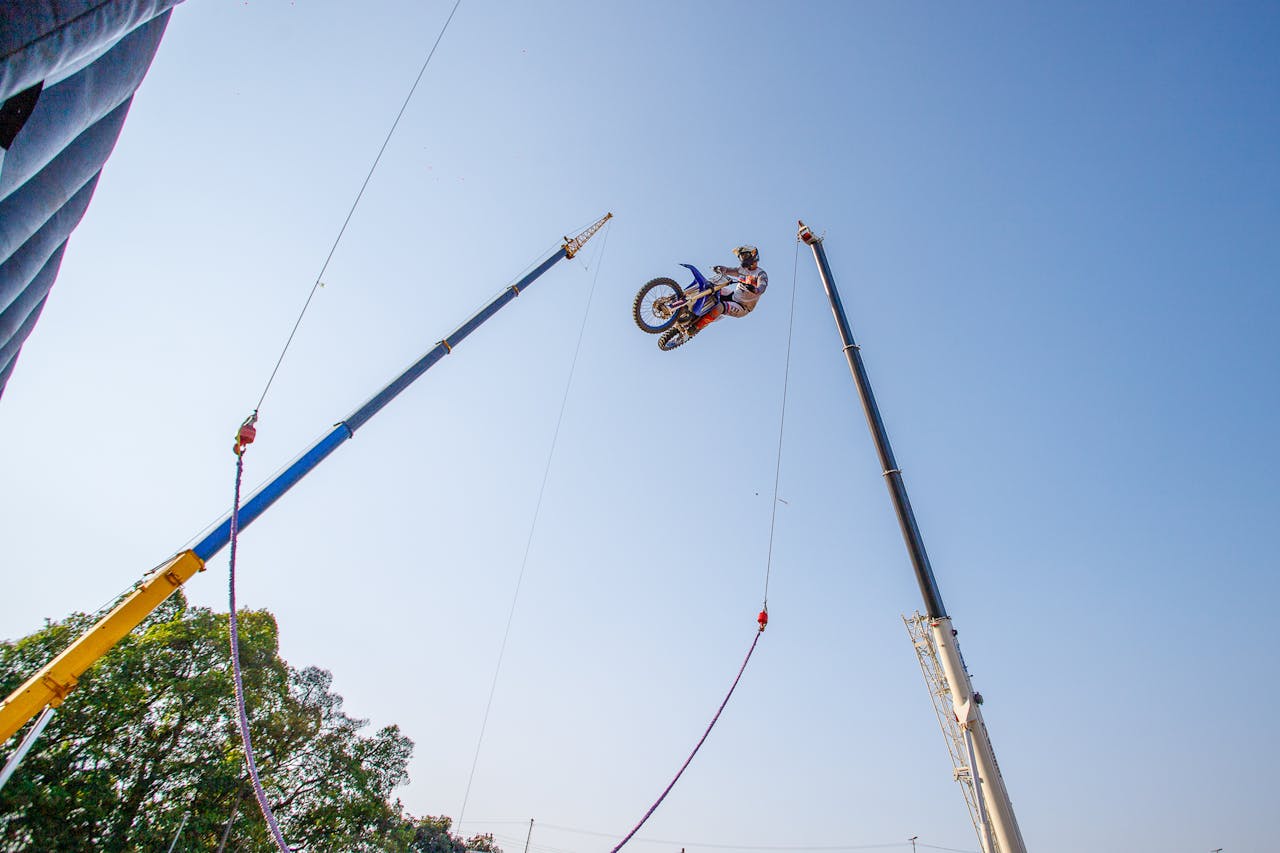Home Daring motocross stunt high in the air between cranes under a clear blue sky.
