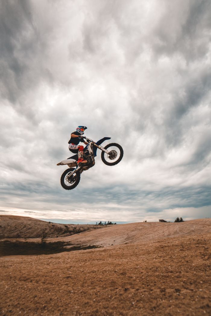 Offerings Unrecognizable male biker in helmet jumping high in air while performing dangerous stunt in field against cloudy sky